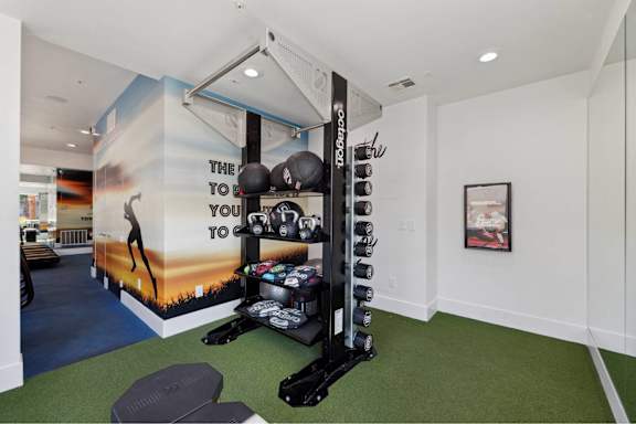 A gym room with a wall mural that says "The way to go" and a rack of weights.
