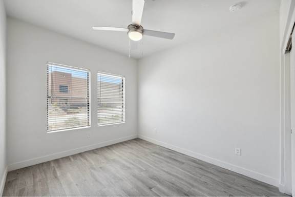 A room with a ceiling fan and two windows.