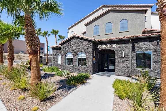 A building with a stone facade and a sign that reads "LEASING CENTER" is surrounded by palm trees and small bushes.