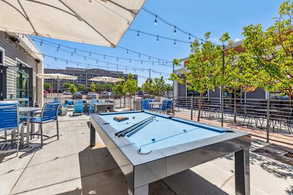 A pool table is in the middle of a patio with chairs and umbrellas.