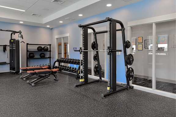 A gym with a variety of equipment including a squat rack, bench, and dumbbells.