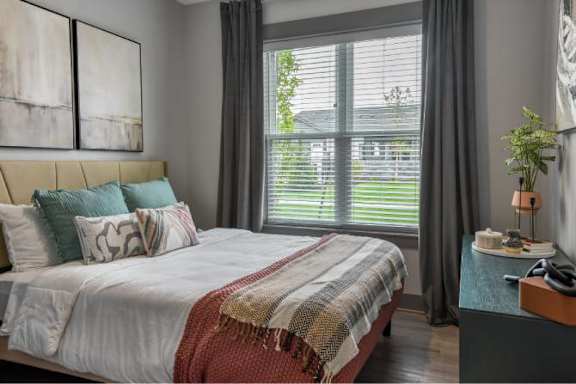 A bedroom with a large bed and a window with blinds.