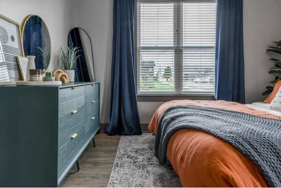 A bedroom with a bed, a dresser, and a window with blinds.