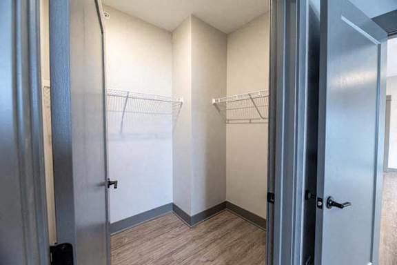 A walk-in closet with a wooden floor and metal doors.