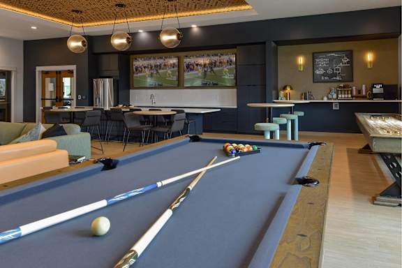 A pool table is in the middle of a room with a bar and seating area.