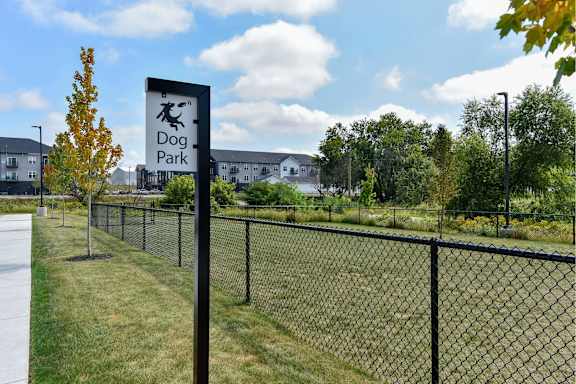 A sign for a dog park stands in front of a fence.