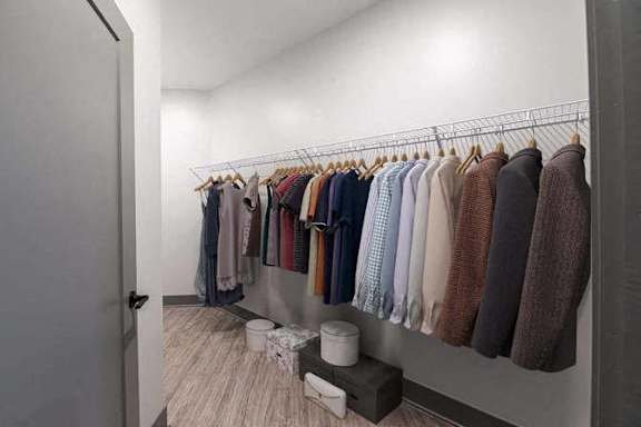 A row of sweaters hang on a rack in a white room.