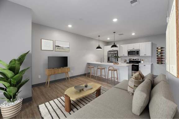 A modern living room with a grey couch, a wooden coffee table, and a kitchen area in the background.