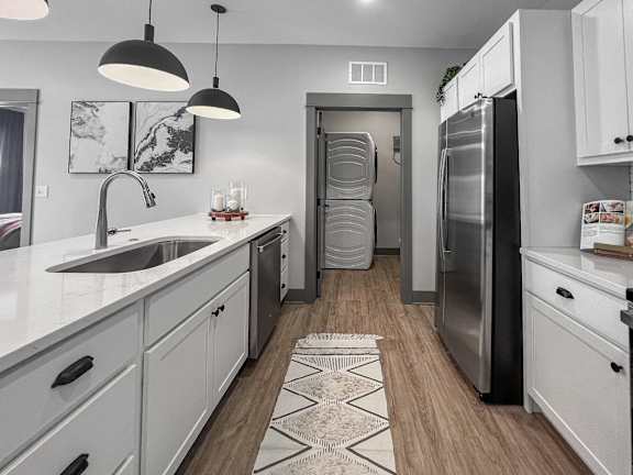 A modern kitchen with a sink, refrigerator, and a patterned rug on the floor.