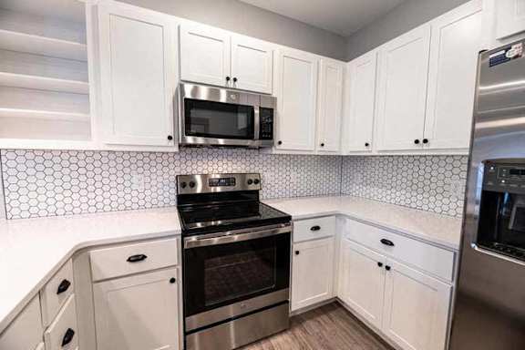 A kitchen with white cabinets and a black and white tiled backsplash.