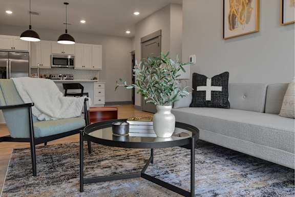 A modern living room with a grey couch, a coffee table, and a kitchen in the background.