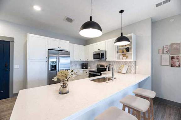 A kitchen with a white countertop and a sink under a hanging light fixture.