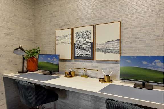 A modern office with a white desk, two monitors, and a chair.
