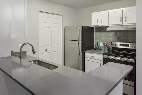 A kitchen with a black refrigerator, white cabinets, and a stainless steel sink.