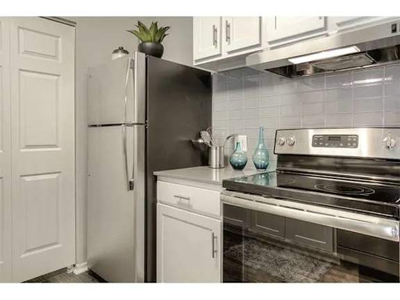 A black refrigerator stands next to a stainless steel oven in a kitchen.