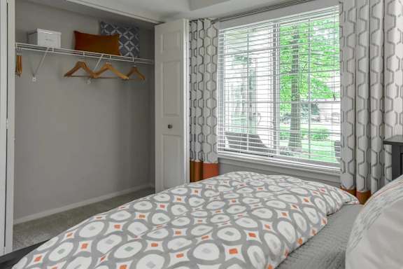 A bedroom with a bed, a window with curtains, and a closet with clothes hanging.