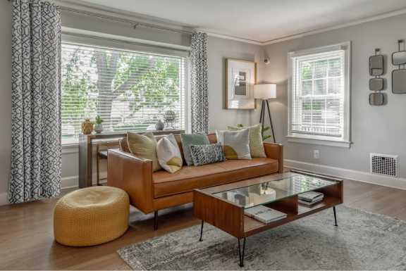 A living room with a brown couch, a glass coffee table, and a yellow pouf.