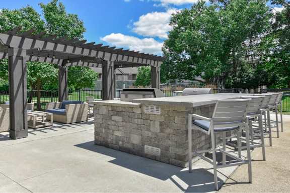 A concrete patio with a stone bar and chairs under a pergola.