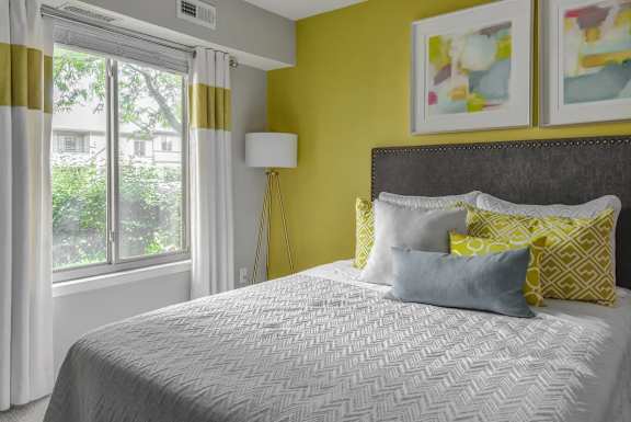 A bedroom with a bed, pillows, a lamp, and two paintings on the wall.