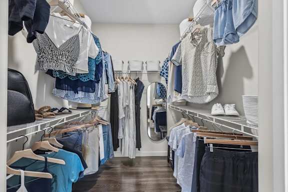 A walk in closet with clothes hanging on shelves and hangers.