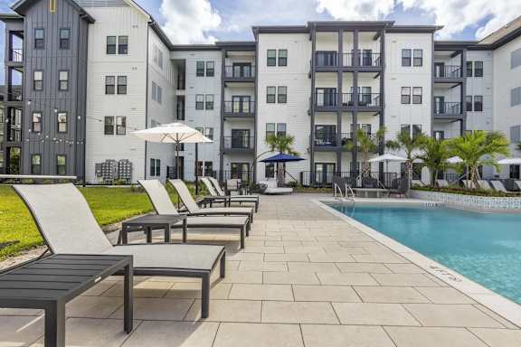 A pool area with lounge chairs and umbrellas in front of apartment buildings.