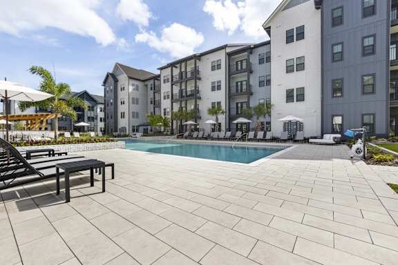 A large outdoor pool area with a tiled floor and a few lounge chairs.