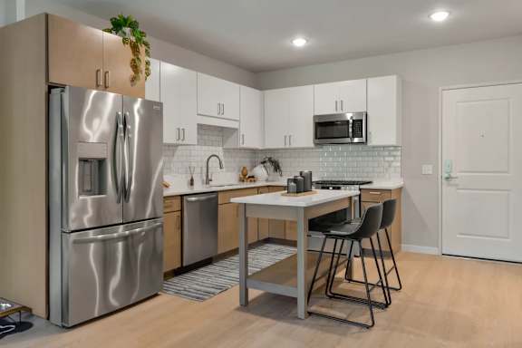 A kitchen with a refrigerator, sink, and a dining table with chairs.