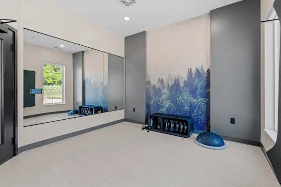 A room with a large painting of a forest on the wall and a blue ottoman in the corner.