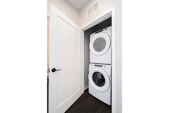 Two washing machines are stacked in a small laundry room.
