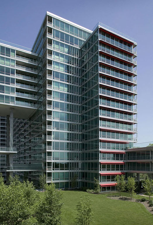 A modern glass building with red accents on the balconies.