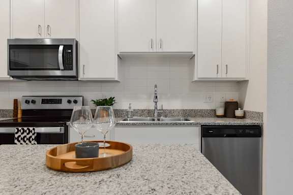 A modern kitchen with a granite countertop and a wooden tray with a candle on it.