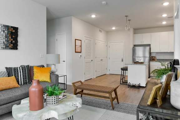 A living room with a grey couch, a coffee table, and a kitchen area in the background.