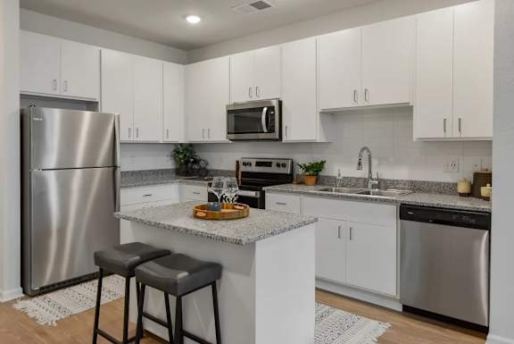 A kitchen with a refrigerator, microwave, and bar stools.