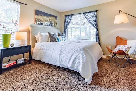 A bedroom with a large bed, a chair, and a painting on the wall.