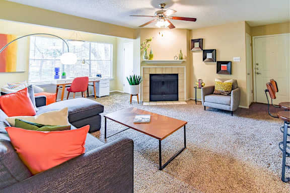 A living room with a grey couch, orange pillows, a coffee table, and a fireplace.