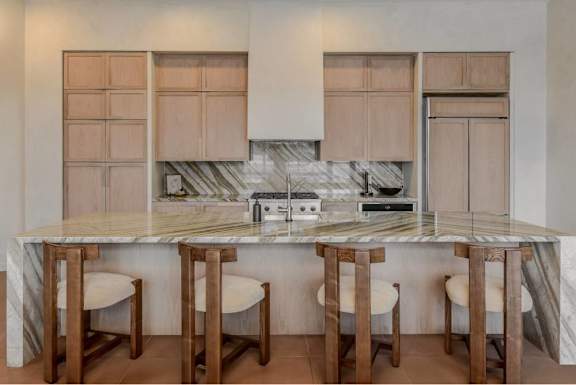 A kitchen with a marble countertop and wooden bar stools.