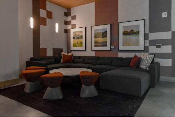 A modern living room with a grey sofa and orange ottoman.