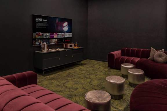 A room with a red couch and ottoman in front of a black wall with a poster on it.