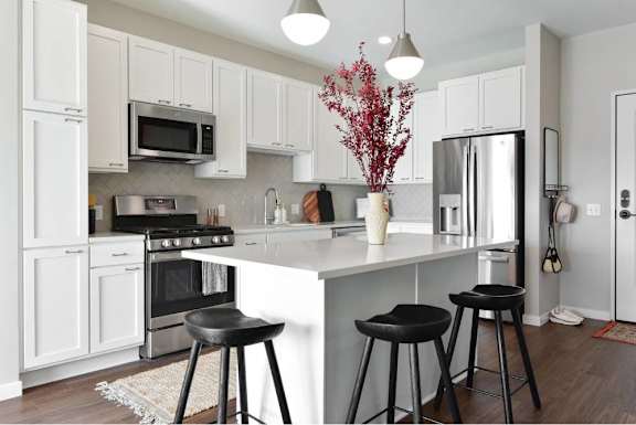 A kitchen with white cabinets and a white island with two black stools.