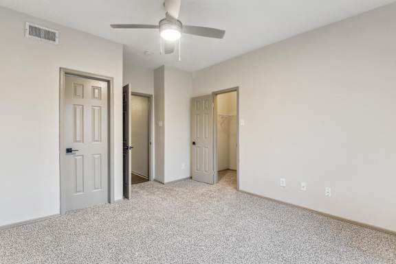 A room with a ceiling fan and three doors.