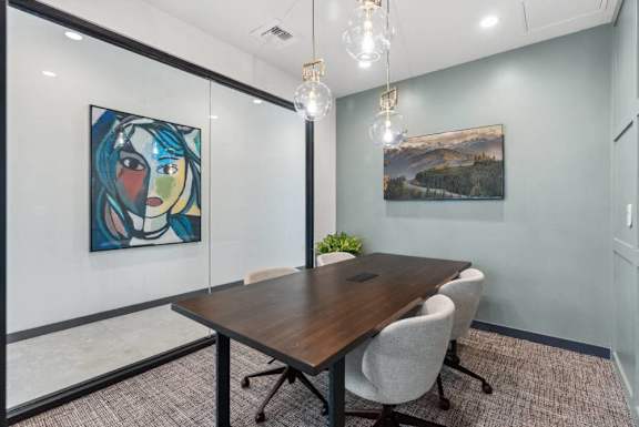 A conference room with a wooden table and chairs, a painting on the wall, and a plant on the table.