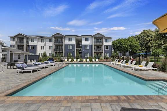 A large swimming pool surrounded by lounge chairs in front of apartment buildings.