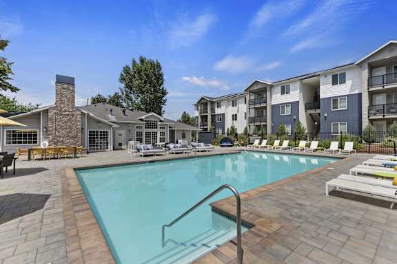 A large swimming pool surrounded by lounge chairs and apartment buildings.