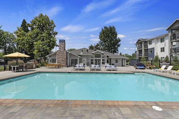 A large swimming pool surrounded by a stone patio and lounge chairs.