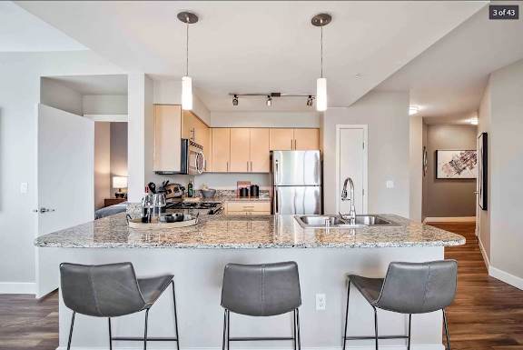 Open kitchen with a counter top with three chairs at The Pacifica Apartments, Tacoma, WA, 98409