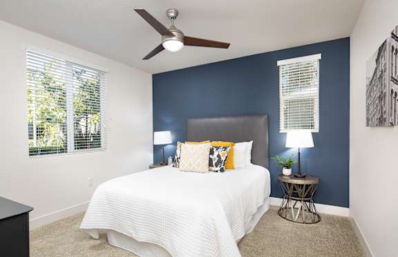 A bedroom with a bed, a ceiling fan, and a window with blinds.