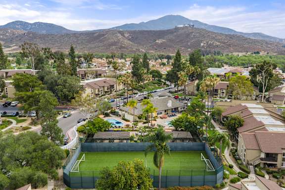 A tennis court is surrounded by houses and trees.