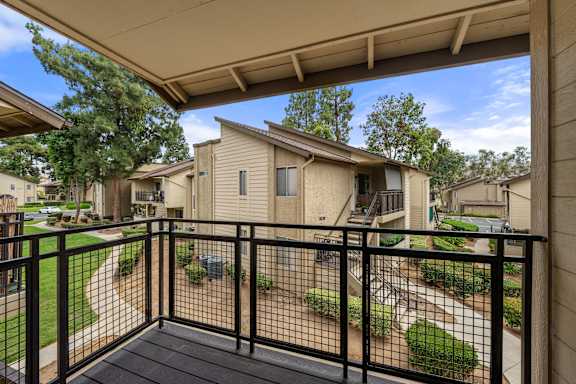 A balcony with a black railing overlooks a residential area.