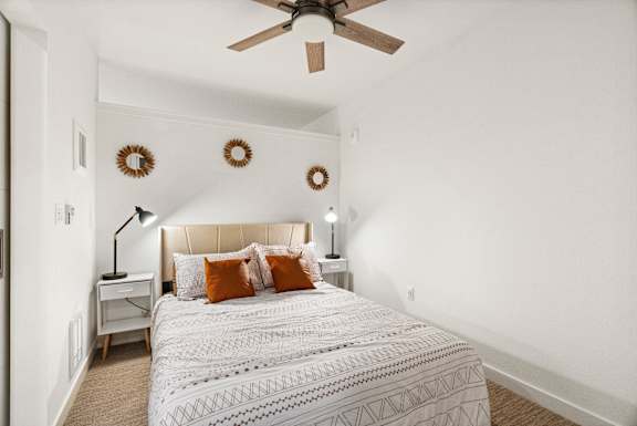 A bedroom with a bed, a ceiling fan, and wall decorations.