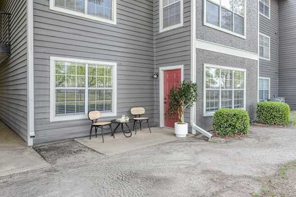 A grey house with a red door and a small table and chairs on the porch.